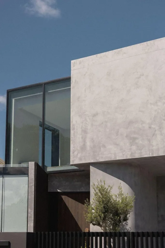 Your Guide to Cement Render: Everything You Need to Know Corner of modern grey house behind a black fence with the tree