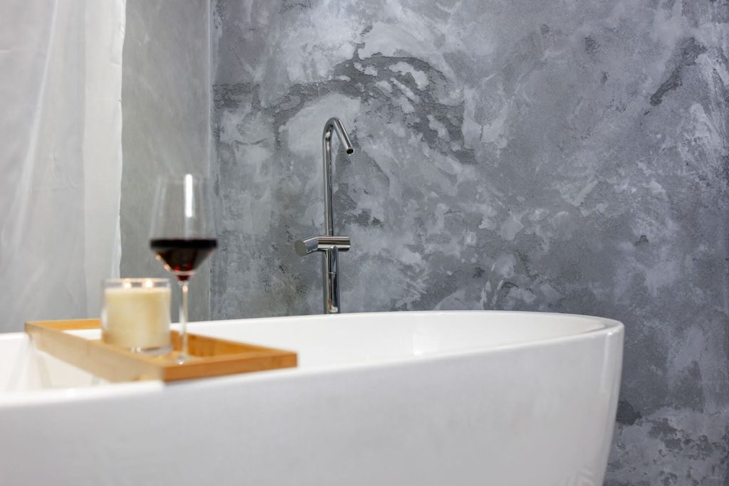 bath with a wooden board with candles and wine in front of a grey stone wall
